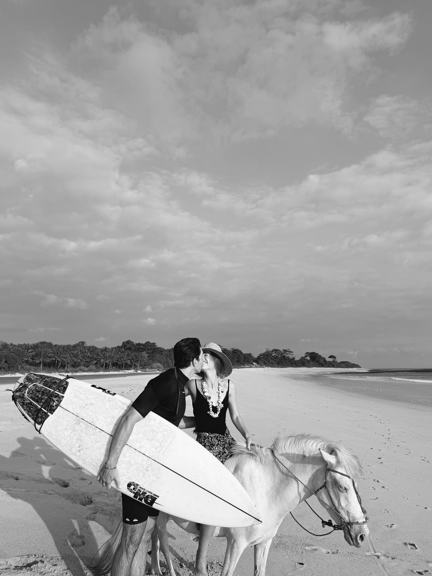 María y Álvaro besándose en la playa junto a un caballo y una tabla de surf