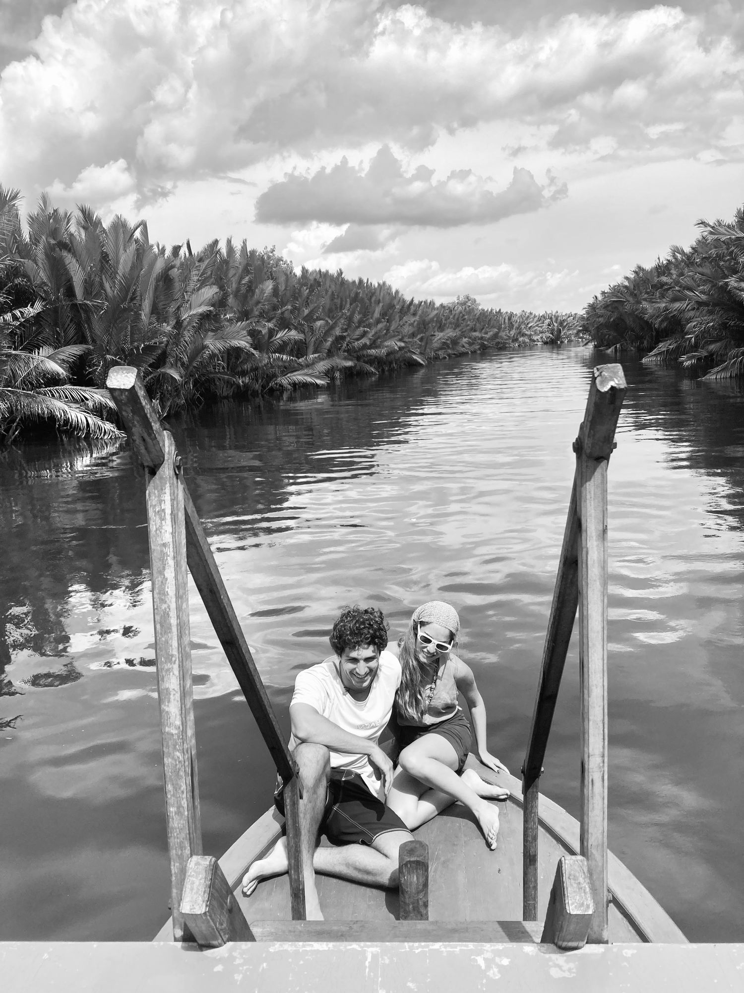 María y Álvaro sentados en la proa de una barca por un río entre palmeras